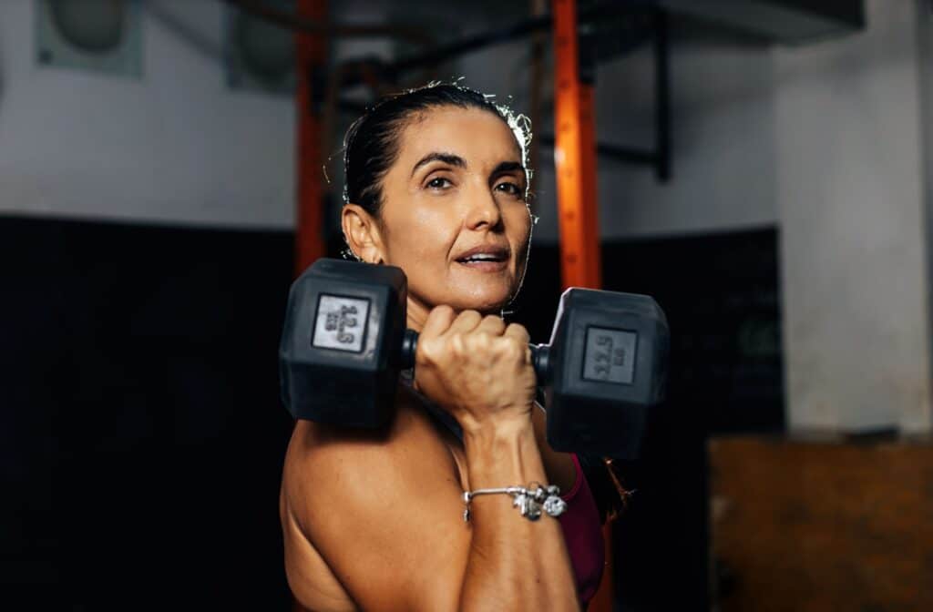 A woman holding a dumbbell at her shoulder during a strength training session.
