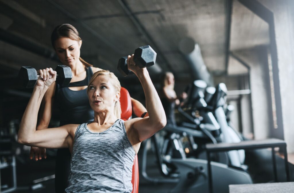 A personal trainer working with a client in a gym who is lifting dumbbells.