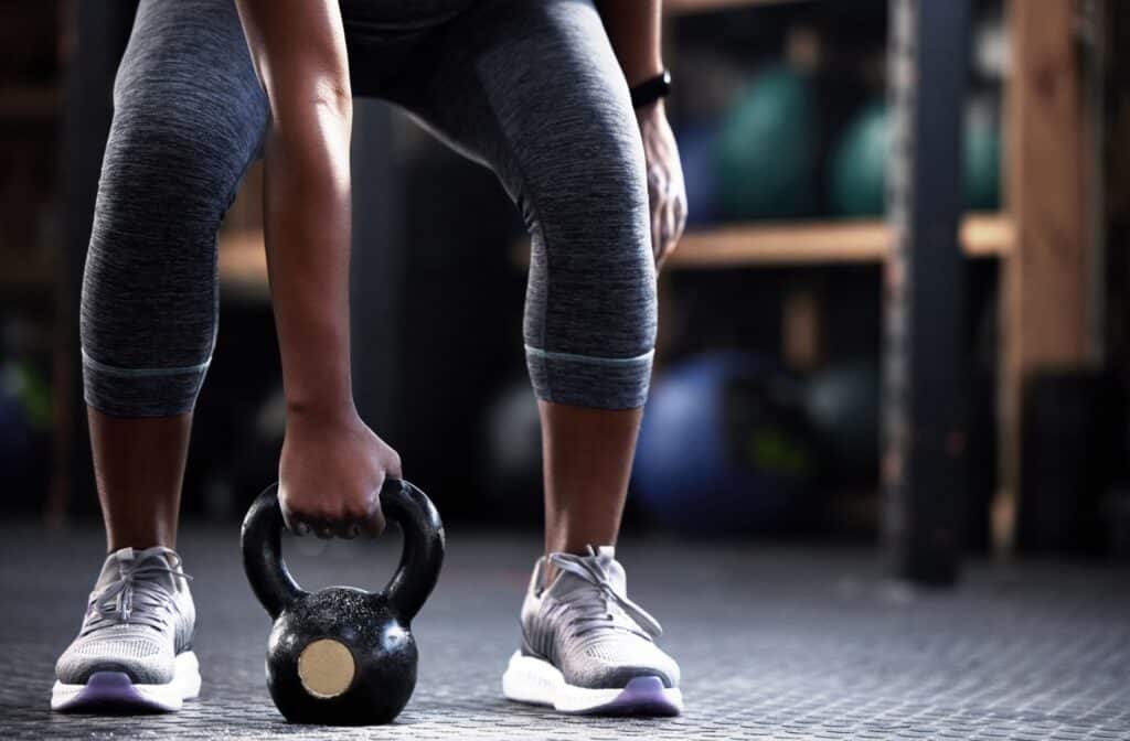 A person holding a kettle bell between their feet while lifting weights during a session at the gym.