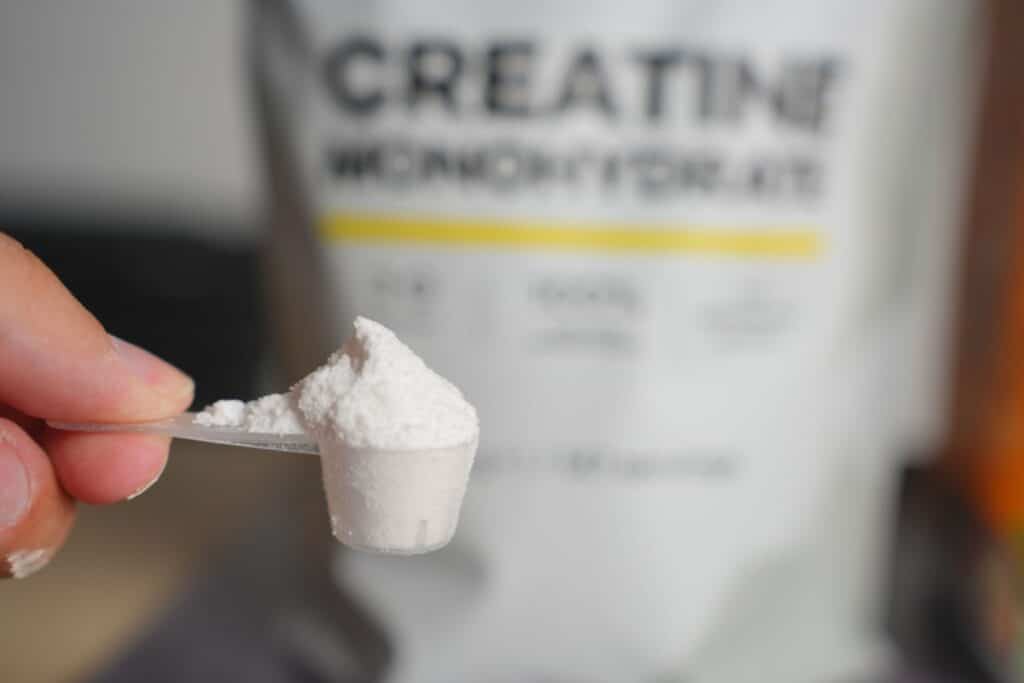 Close-up of hand holding measuring scoop filled with white creatine powder.